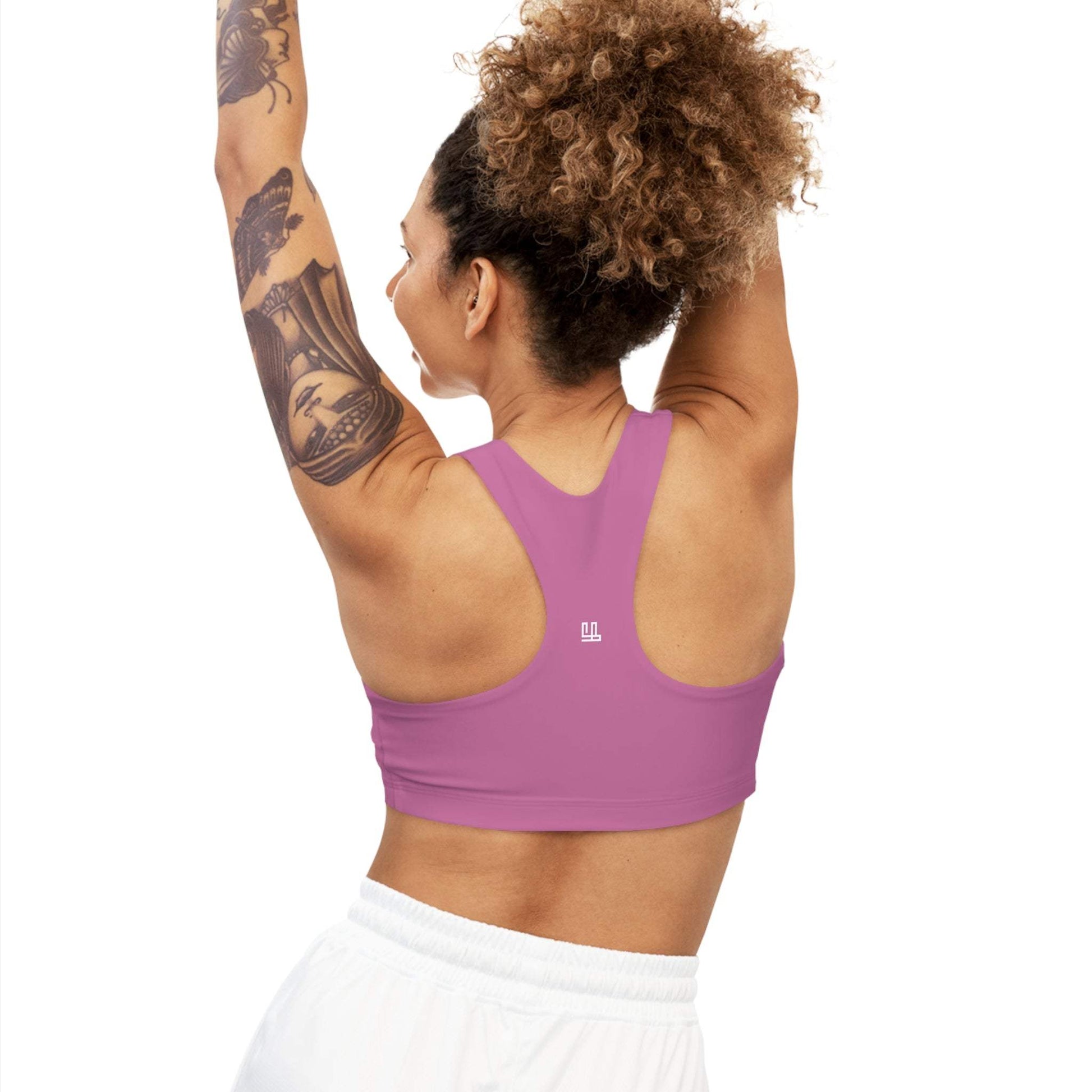 Seamless Sports Bra Fearlessli worn by tattooed woman with arms raised, showcasing pink color and racerback design.